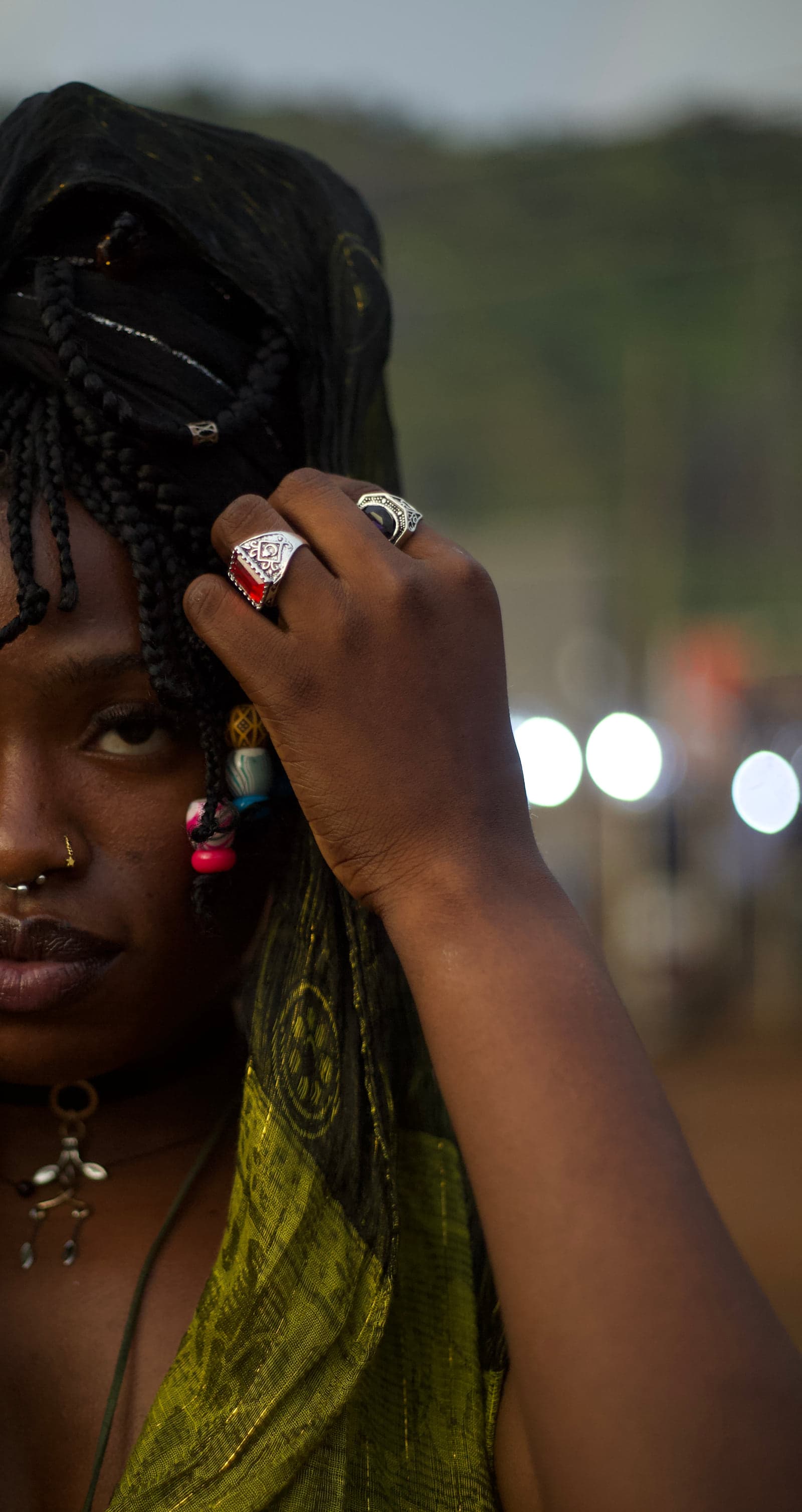 A close-up of an artist, half in frame, with silver rings on the hand raised to beaded braids.